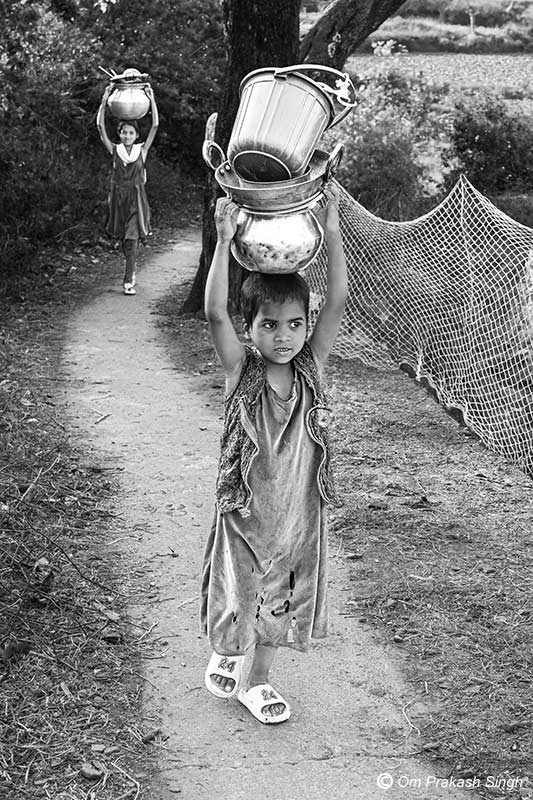 A very young girl child hauling water and clean utensils from a distant water source in Khunti district, Jharkhand, India